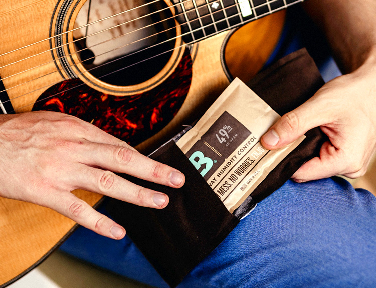 Person holding an acoustic guitar placing a Boveda pack in a fabric holder