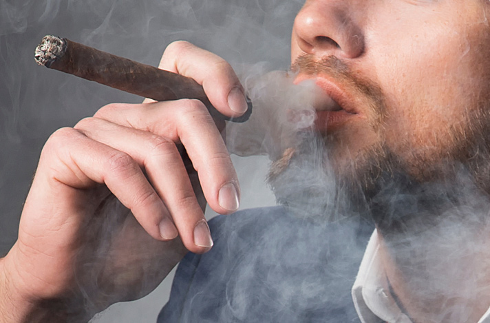 Close-up of a bearded man smoking cigar holding the cigar in a pen type positioning