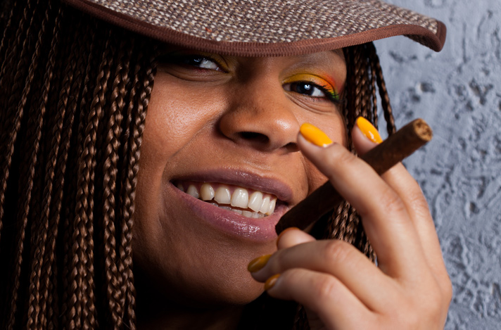 Close up of a smiling woman holding a cigar in a scissors type hand positioning