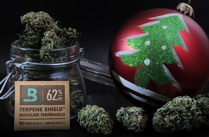 Glass jar of cannabis buds, a 62% RH size 8 Boveda, random individual buds and a Christmas ornament.