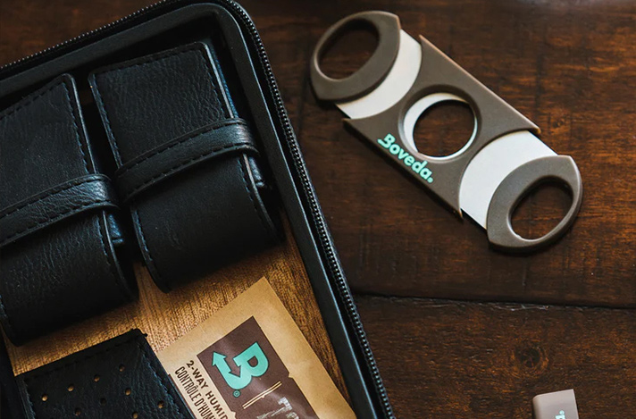 Boveda cigar cutter and Boveda 72% size 8 humidification pack pictured on a table with a leather cigar case.
