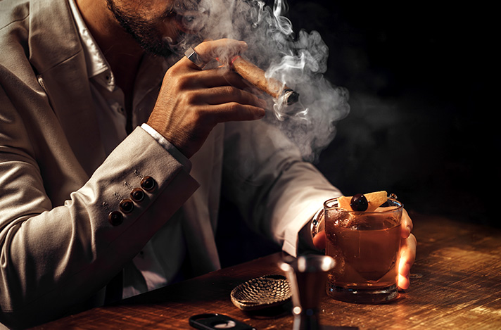 Man smoking a lit cigar with an old fashioned drink.