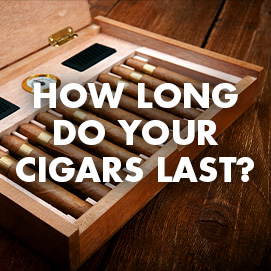 A humidor full of cigars on a wood table top with the blog title 