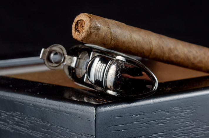 A single cigar with a punch in the cap along with a cigar punch device sitting on a humidor box.