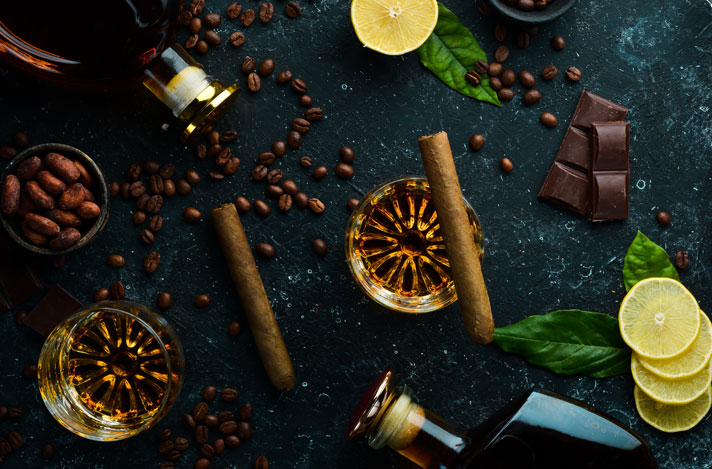 A cigar on a table top with coffee, chocolate, and lemons around