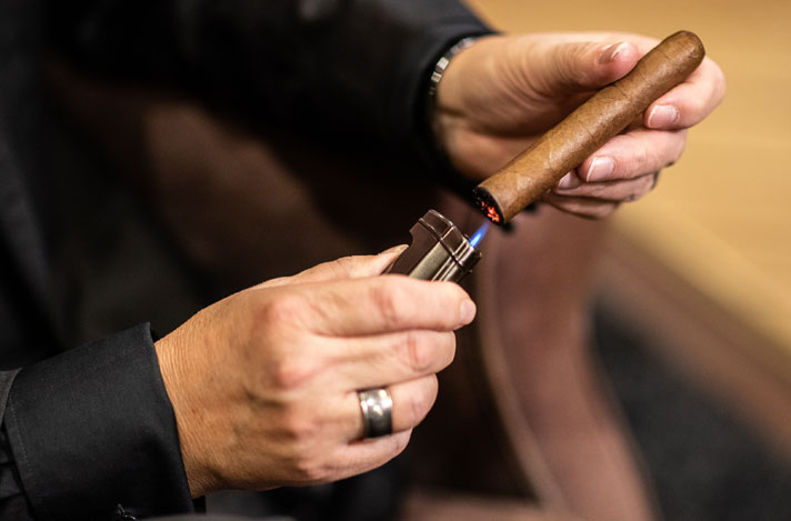 A man lighting a cigar with a torch lighter