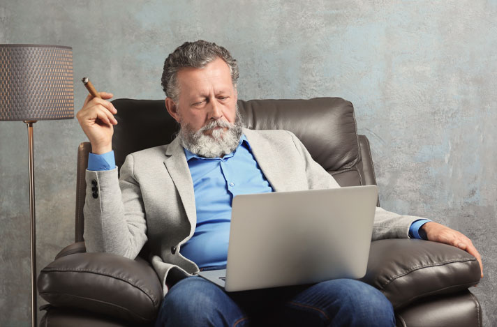 A man sitting on a couch with a laptop and a cigar