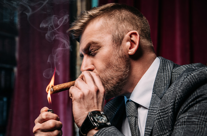 An English man dressed nicely in a cigar bar lighting a cigar.