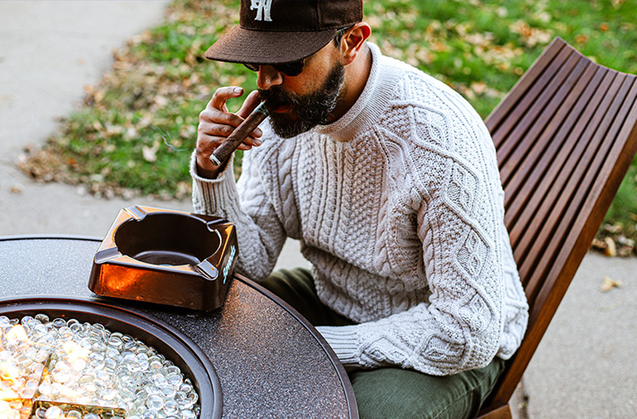 A man smoking a cigar outside by a fire pit