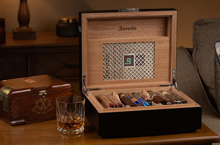 The Boveda Humidor full of cigars on a table with a whisky glass